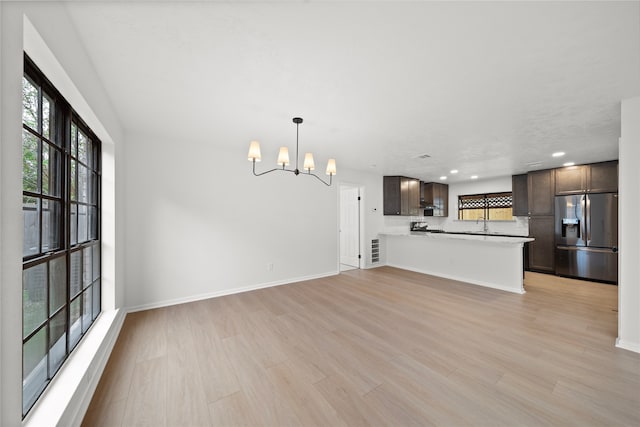 kitchen featuring kitchen peninsula, hanging light fixtures, stainless steel fridge with ice dispenser, a notable chandelier, and dark brown cabinetry