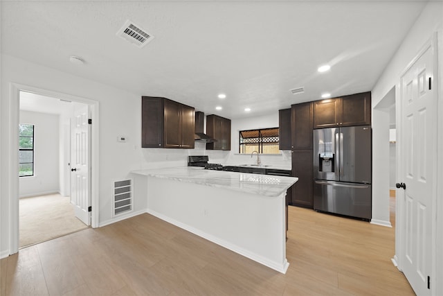 kitchen with kitchen peninsula, stainless steel refrigerator with ice dispenser, wall chimney exhaust hood, black range oven, and sink