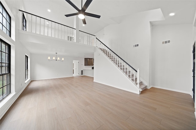 unfurnished living room with a towering ceiling, light hardwood / wood-style floors, and ceiling fan with notable chandelier