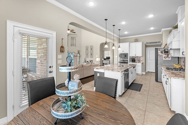 kitchen with pendant lighting, light stone counters, tasteful backsplash, an island with sink, and white cabinets