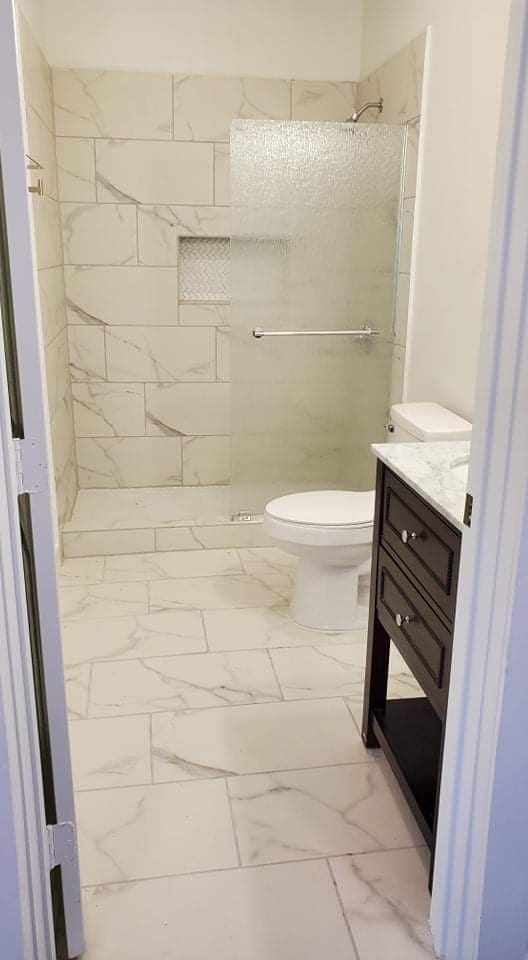 bathroom with toilet, a tile shower, and vanity