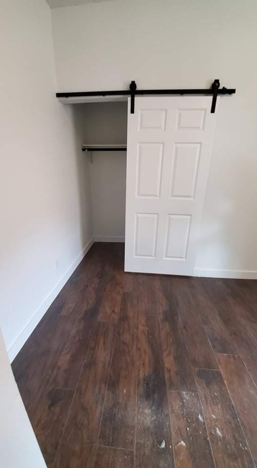 unfurnished bedroom featuring dark wood-type flooring and a barn door