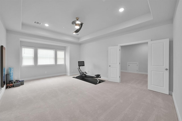 exercise room with baseboards, a tray ceiling, visible vents, and light colored carpet