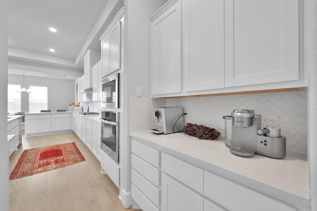 kitchen featuring appliances with stainless steel finishes, a raised ceiling, white cabinetry, and light wood-style flooring