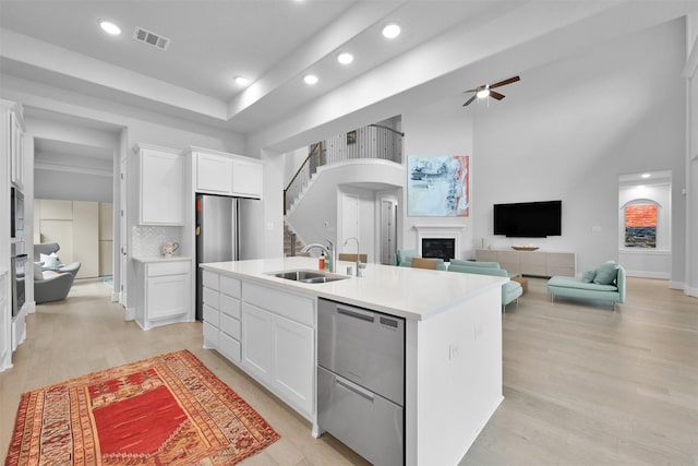 kitchen featuring a sink, visible vents, white cabinets, an island with sink, and a glass covered fireplace