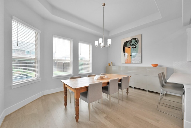 dining area with a chandelier, a raised ceiling, baseboards, and light wood finished floors