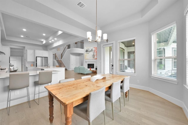 dining room featuring a fireplace, visible vents, baseboards, light wood-style floors, and a tray ceiling