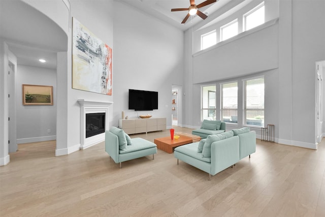 living room featuring a ceiling fan, a glass covered fireplace, light wood-style flooring, and baseboards