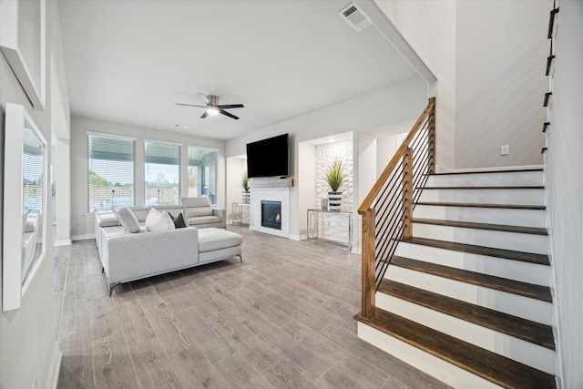 living room featuring ceiling fan, a fireplace, and light hardwood / wood-style flooring