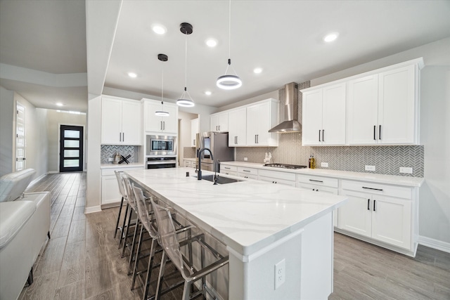 kitchen with light wood-type flooring, wall chimney exhaust hood, stainless steel appliances, and white cabinets