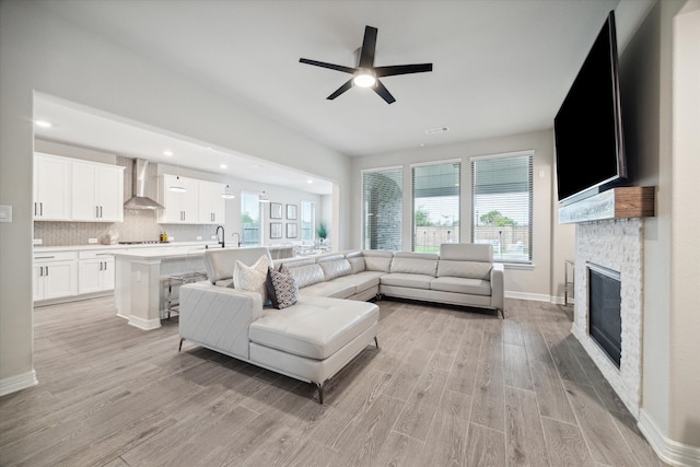 living room with a stone fireplace, sink, ceiling fan, and light hardwood / wood-style floors