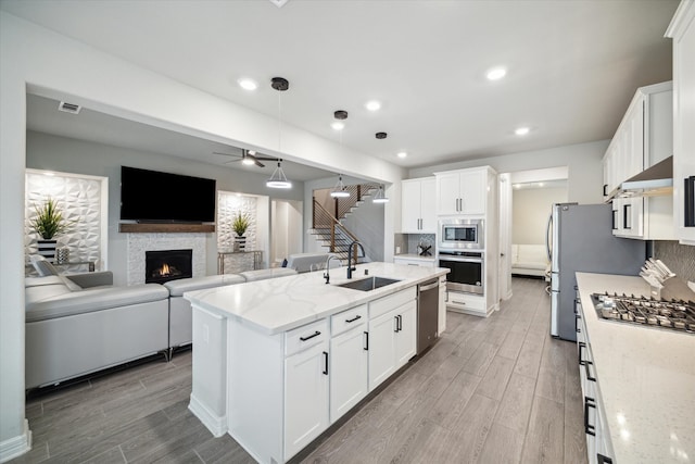 kitchen featuring a stone fireplace, appliances with stainless steel finishes, sink, hardwood / wood-style flooring, and white cabinets