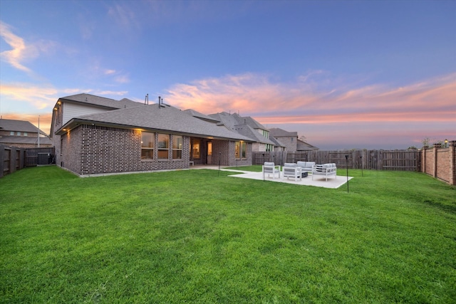 back house at dusk with a patio area, a yard, and central AC