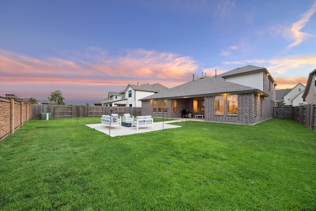 back house at dusk featuring a lawn and a patio