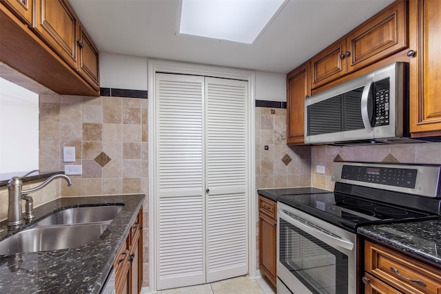 kitchen featuring appliances with stainless steel finishes, decorative backsplash, dark stone countertops, light tile patterned floors, and sink