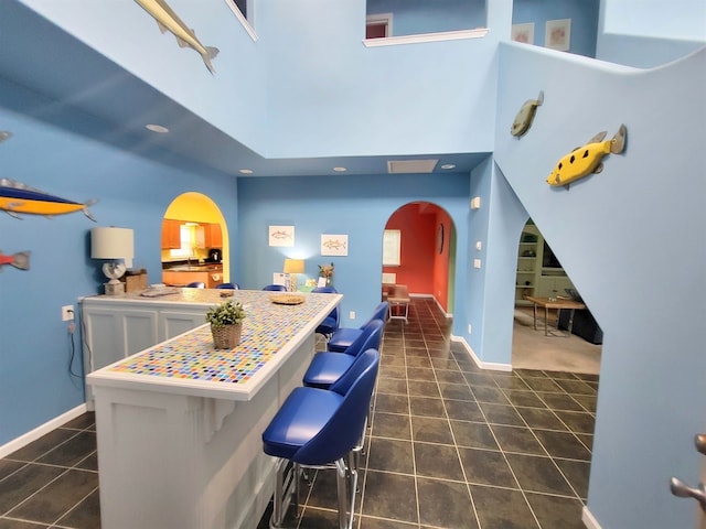 kitchen with dark tile patterned flooring, a towering ceiling, kitchen peninsula, and a breakfast bar