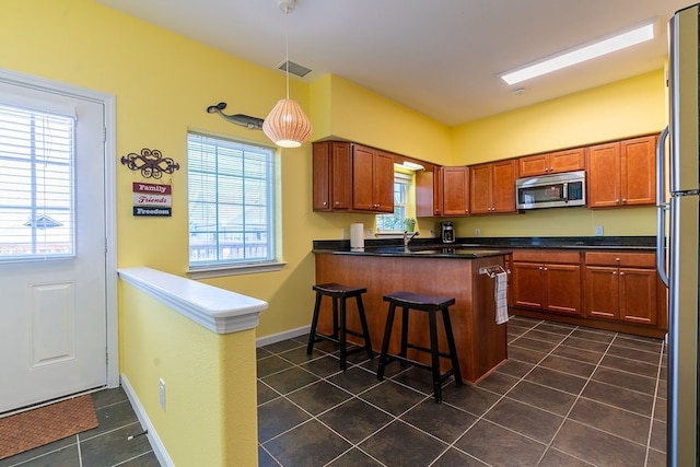 kitchen featuring decorative light fixtures, kitchen peninsula, dark tile patterned floors, appliances with stainless steel finishes, and a breakfast bar area