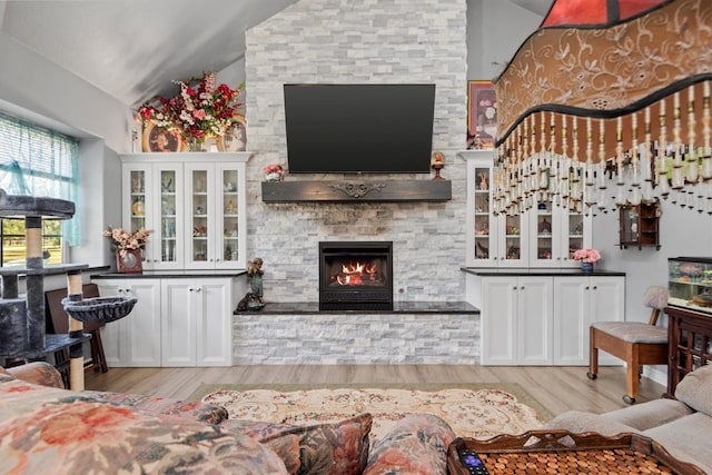 living room featuring light wood-type flooring, a fireplace, and vaulted ceiling