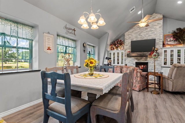 dining area featuring a fireplace, vaulted ceiling, ceiling fan with notable chandelier, and hardwood / wood-style flooring