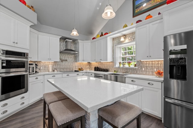 kitchen featuring lofted ceiling, hanging light fixtures, appliances with stainless steel finishes, and wall chimney exhaust hood