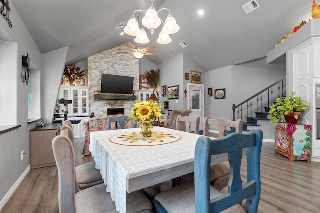 dining area with ceiling fan with notable chandelier, dark hardwood / wood-style floors, vaulted ceiling, and a stone fireplace