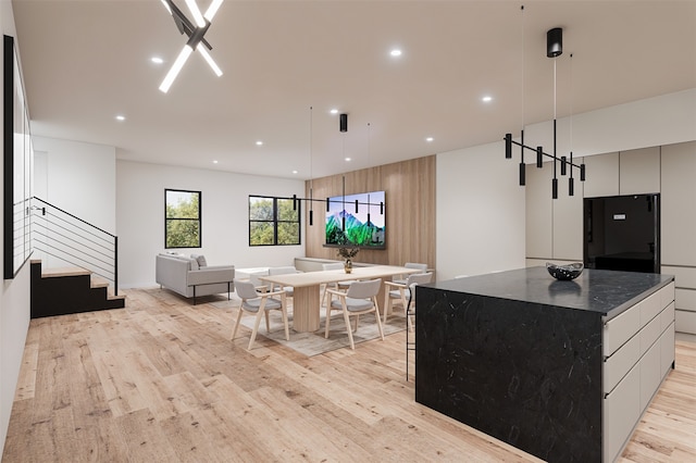 kitchen with black fridge, a kitchen island, light hardwood / wood-style flooring, white cabinetry, and dark stone countertops