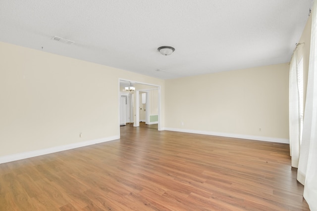 empty room featuring a textured ceiling, hardwood / wood-style flooring, and an inviting chandelier