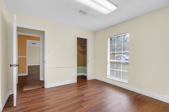 unfurnished bedroom featuring a textured ceiling, dark hardwood / wood-style floors, a closet, and a walk in closet