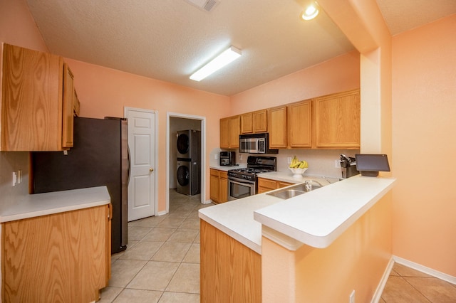 kitchen featuring light tile patterned floors, appliances with stainless steel finishes, stacked washer and clothes dryer, sink, and kitchen peninsula