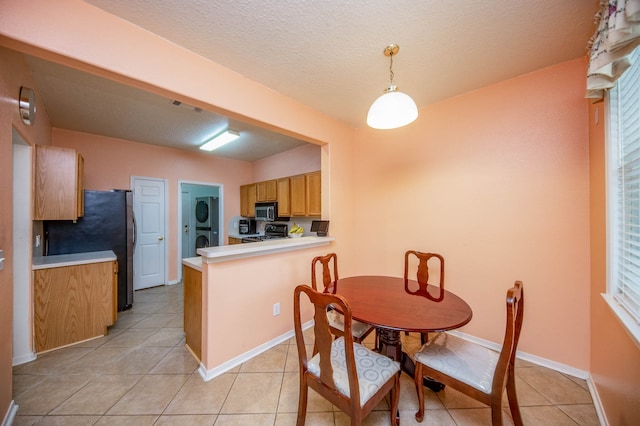 dining space with a textured ceiling, stacked washer and clothes dryer, and light tile patterned flooring