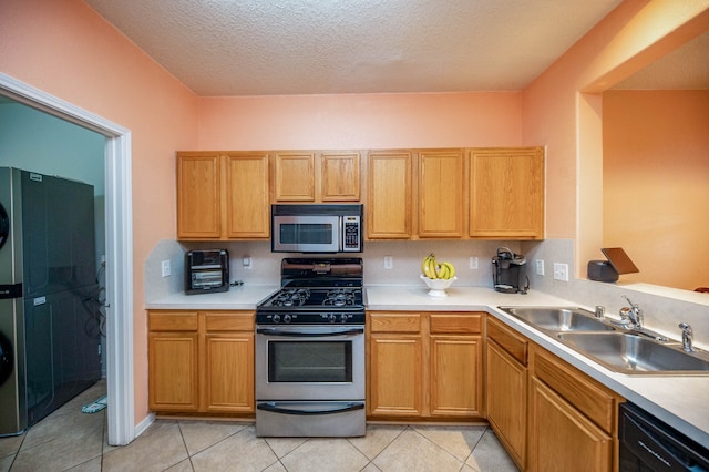 kitchen with a textured ceiling, stainless steel appliances, sink, stacked washer / dryer, and light tile patterned flooring