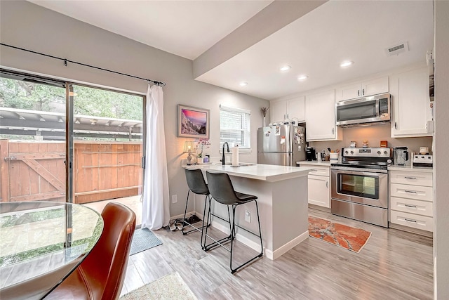 kitchen with a breakfast bar, kitchen peninsula, light wood-type flooring, appliances with stainless steel finishes, and white cabinetry