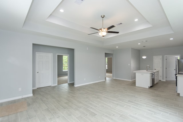 unfurnished living room featuring sink, a tray ceiling, light hardwood / wood-style floors, and ceiling fan