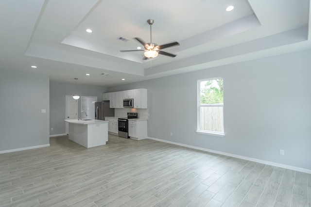 unfurnished living room featuring light hardwood / wood-style floors, sink, and a tray ceiling