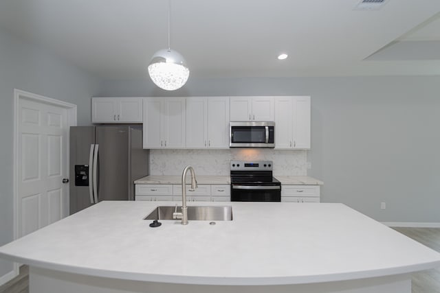 kitchen with sink, hanging light fixtures, white cabinetry, stainless steel appliances, and a kitchen island with sink