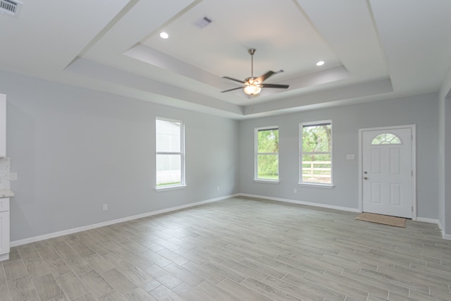 unfurnished living room with light hardwood / wood-style floors, a tray ceiling, and ceiling fan