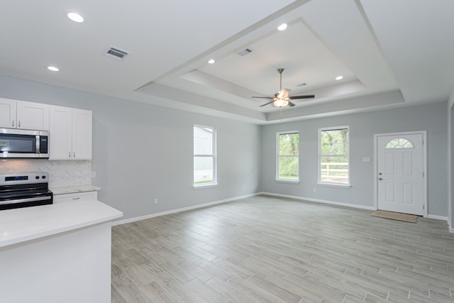 kitchen with appliances with stainless steel finishes, a raised ceiling, white cabinetry, ceiling fan, and light hardwood / wood-style flooring