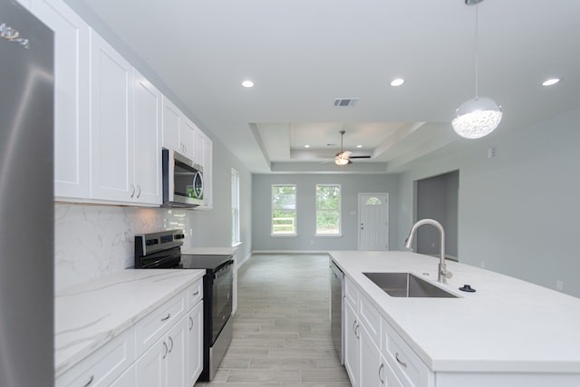 kitchen with a center island with sink, a raised ceiling, appliances with stainless steel finishes, sink, and decorative light fixtures