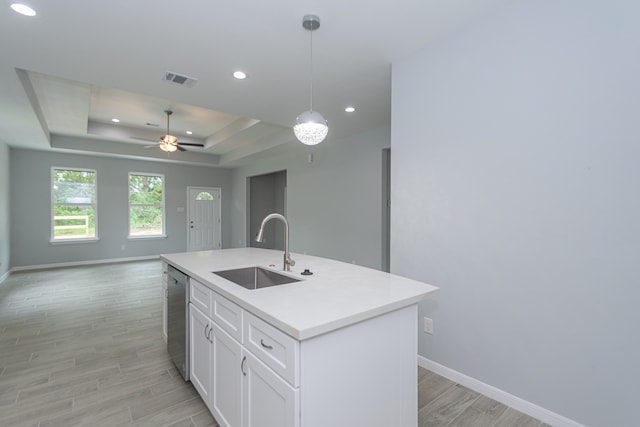 kitchen with hanging light fixtures, a kitchen island with sink, a tray ceiling, dishwasher, and sink