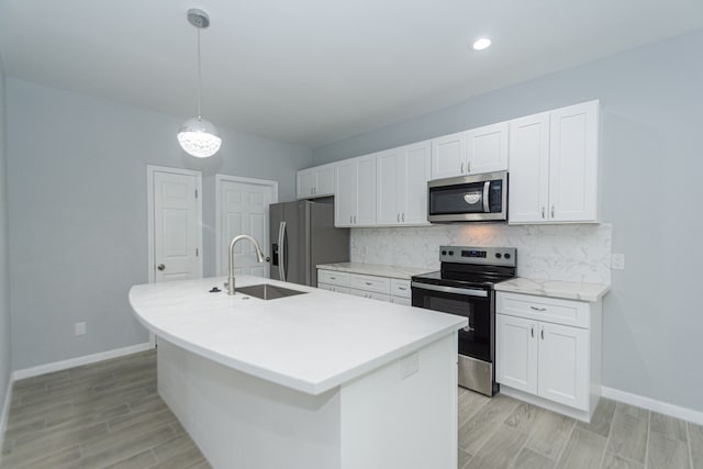 kitchen featuring a center island with sink, sink, white cabinets, pendant lighting, and appliances with stainless steel finishes