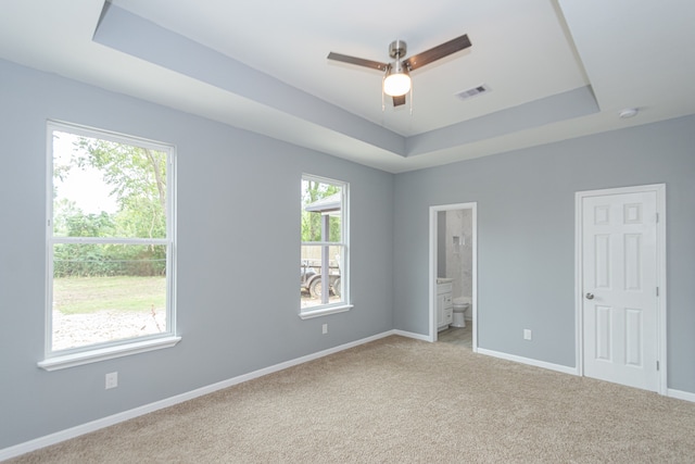 unfurnished bedroom featuring ensuite bathroom, a raised ceiling, multiple windows, and ceiling fan