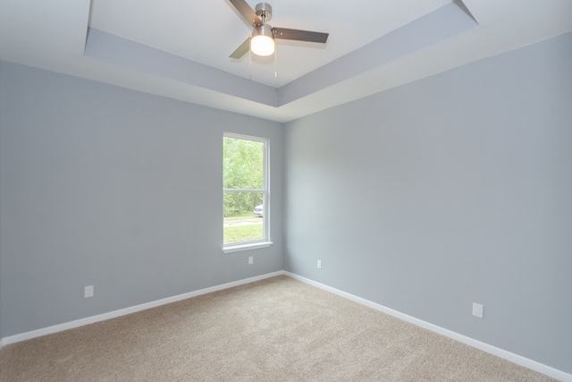 carpeted empty room with ceiling fan and a raised ceiling