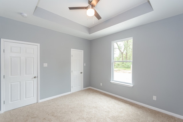 carpeted spare room with ceiling fan and a raised ceiling