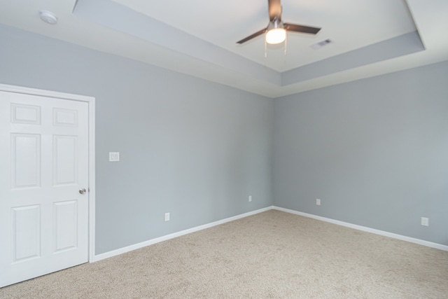 carpeted spare room featuring a tray ceiling and ceiling fan