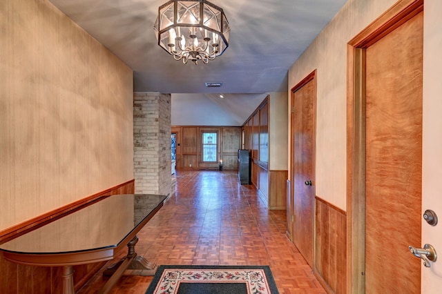 hall with an inviting chandelier, wooden walls, and parquet flooring