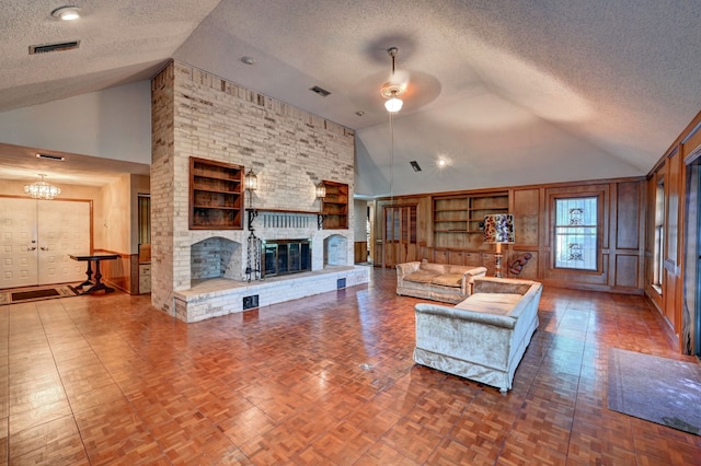 living room featuring ceiling fan with notable chandelier, high vaulted ceiling, a brick fireplace, and a textured ceiling