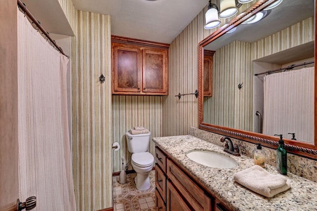 bathroom featuring toilet, wallpapered walls, and vanity