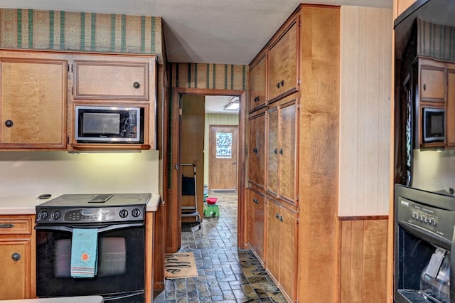 kitchen featuring brown cabinetry, wallpapered walls, brick floor, black electric range, and stainless steel microwave