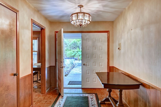 foyer entrance featuring an inviting chandelier, wooden walls, and parquet flooring