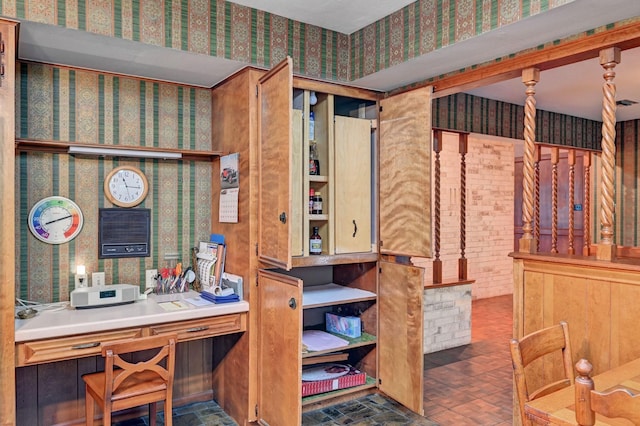 office area with wallpapered walls and brick floor